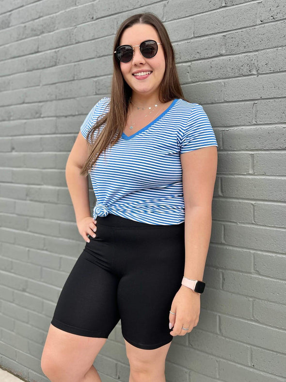 Woman leaning against a brick wall wearing a tied stripped blue tee with Miik's Raven biker shorts in black