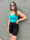 Woman smiling and looking away while leaning against a brick wall wearing Miik's Raven high waisted biker shorts in black with Lori top in ocean 