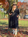 Woman smiling while leaning against to a tree wearing Miik's Rebel midi flounce dresss with pockets in black with boots, a hat and sunglasses 