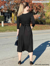 Woman standing with her back towards the camera showing the back of Miik's Rebel midi flounce dress with pockets in black with a black belt