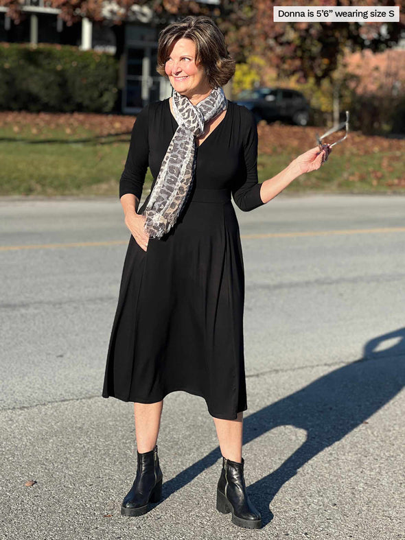 Woman smiling and looking away wearing Miik's Rebel midi flounce dresss with pockets in black with a matching colour boots and a animal print scarf