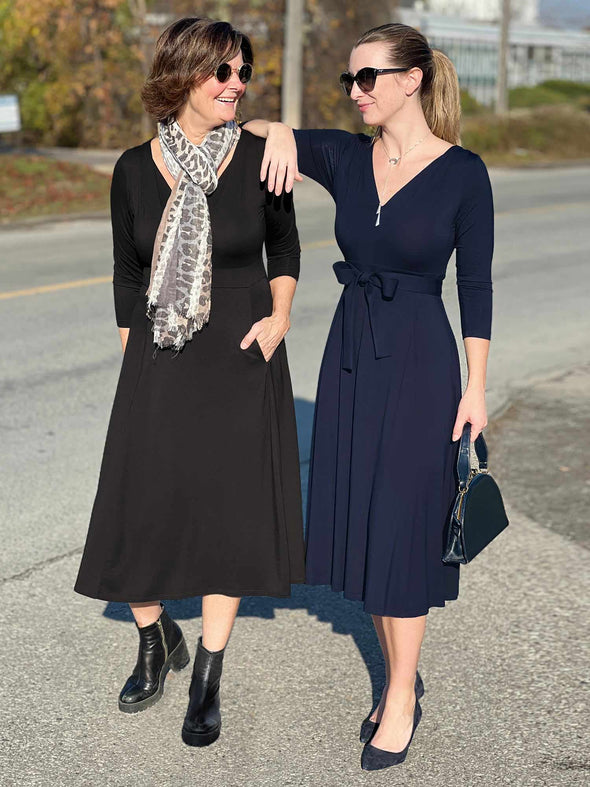 Two women looking to each other and smiling while wearing Miik's Rebel midi flounce dresss with pockets in black and navy melange 