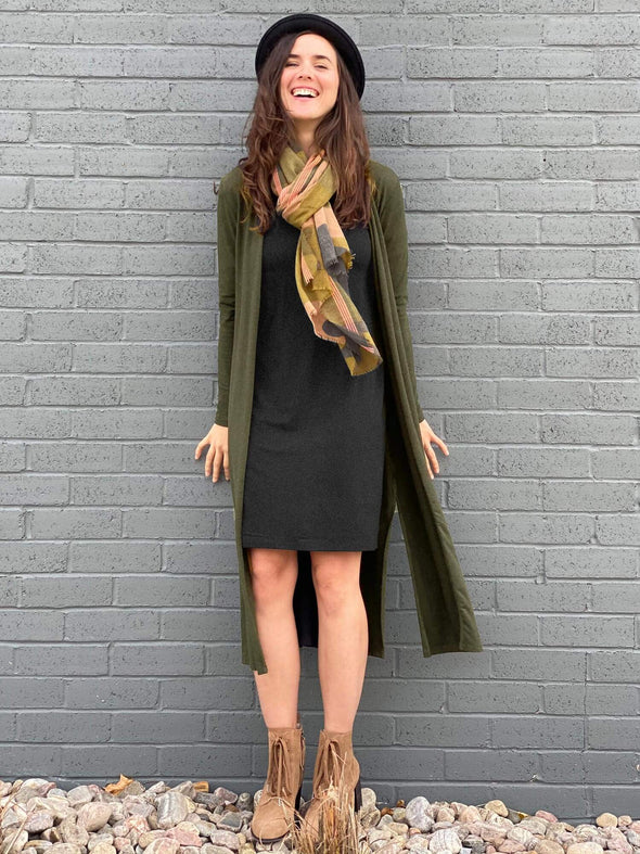 Woman standing in front of a wall wearing Miik's Yara reversible boat/scoopneck dress in grey under a green duster cardigan.
