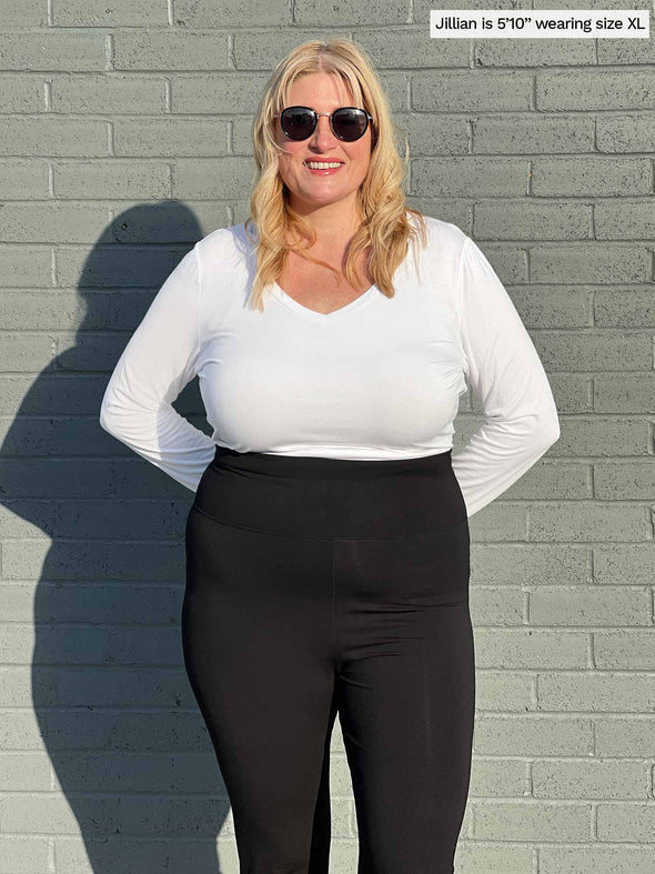 Woman standing in front of a brick wall wearing Miik's Sarvi long sleeve v neck tee in white tucked in a black legging