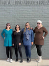 Group of women smiling while standing in front of a brick wall all wearing different colours of Miik's Saya tunic with pockets: teal melange, black, navy melange and chocolate melange 