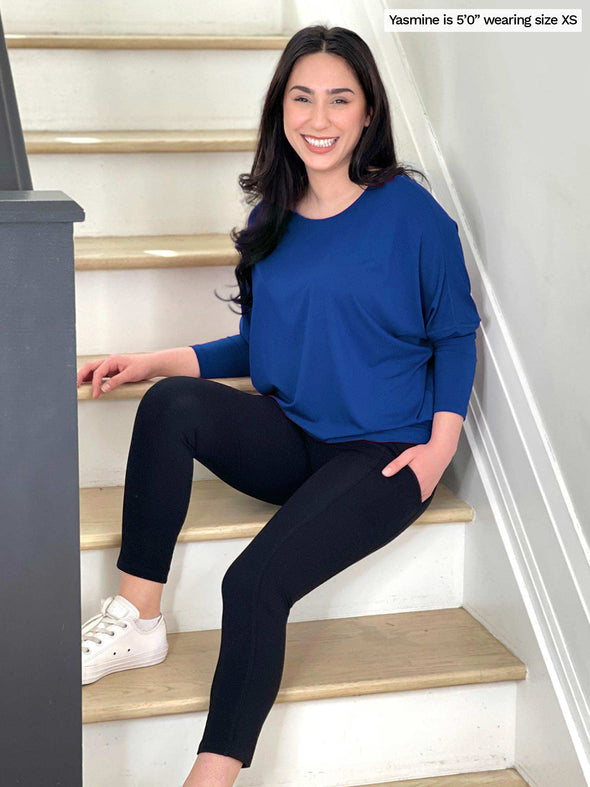 Woman smiling sitting on the stairs wearing Miik's Seana high waisted pocket capri legging in black with a blue long sleeve top