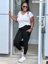 Woman opening a door wearing Miik's Seana high waisted pocket capri legging in black with a white t-shirt. 