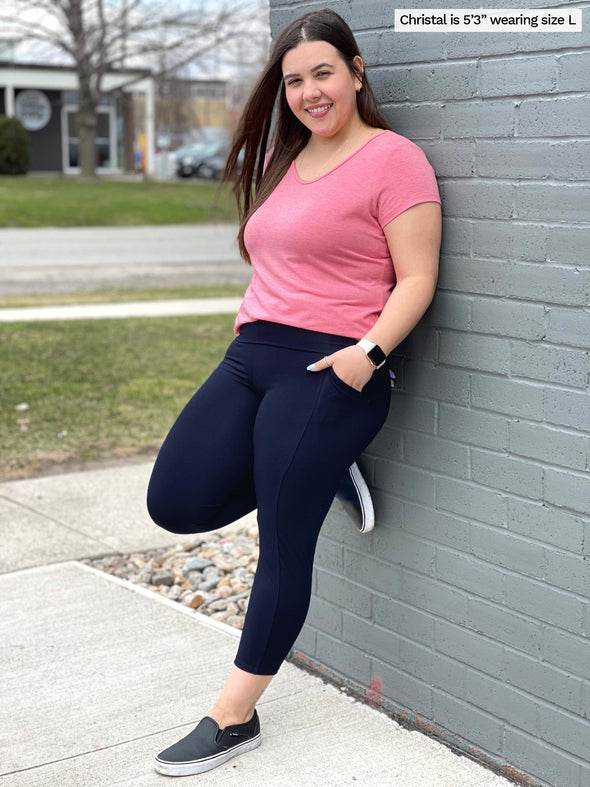 Woman leaning on a wall wearing Miik's Seana high waisted pocket capri legging in navy with a pink t-shirt.