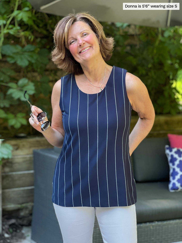 Woman standing in front of outdoor couch smiling wearing Miik's Shane reversible button-up top in navy stripe reversed and pairing it with white jeans.