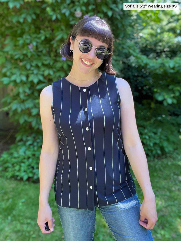 Woman standing in nature smiling wearing Miik's Shane reversible button-up top in navy stripe with blue jeans.