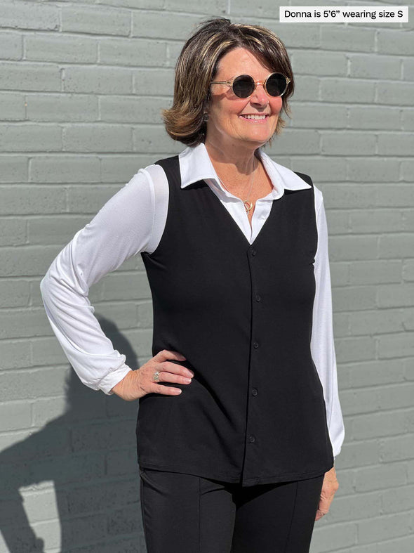 Miik founder Donna standing in front of a grey brick wall with her hand on her hip wearing the Shane button up top styled as a vest over the Lucia collared top.