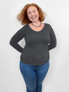 Woman smiling standing in front of a white wall wearing Miik's Shannon long sleeve reversible tee in slate grey and jeans