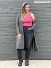 Woman smiling and looking away in front of a brick wall wearing jeans along with a tank top in pink  and Miik's Shevan long cardi in granite melange 