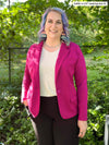 Woman standing in nature smiling while wearing Miik's Sienna girlfriend blazer in pink sangria colour with white top and black pants.