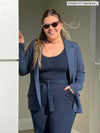 Woman smiling standing next to a wall wearing Miik's Sienna girlfriend blazer in navy melange with a all navy outfit and sunglasses