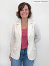 Woman smiling standing in front of a white wall wearing Miik's Sienna girlfriend blazer in oatmeal with a pink pomegranate top and blue jeans 