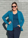 Woman standing in front of a wall wearing Miik's Sienna girlfriend blazer in teal melange with navy pants.