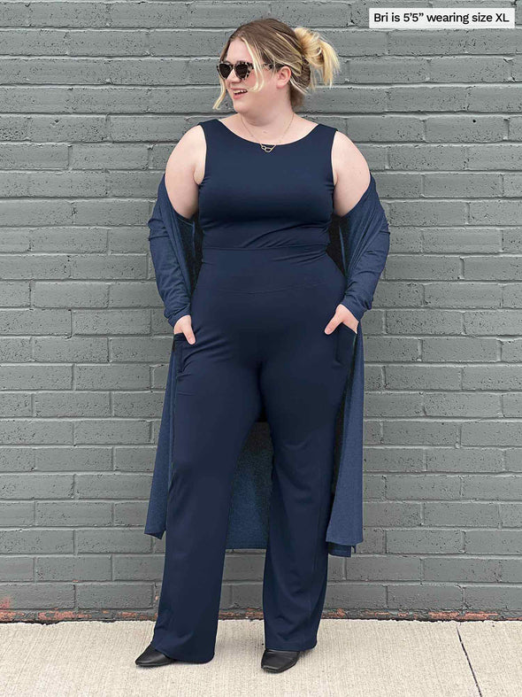 Woman standing in front of a brick wall wearing an all navy outfit: Miik's Sierra pocket pant, Liam top and Shevan long cardigan