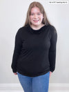 Woman smiling wearing Miik's Sigourney asymmetrical drape neck top in black along with a blue jeans 