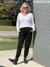 Woman leaning against a brick wall wearing Miik's Silvie slouch pant in black with a long sleeve v neck top in white