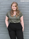 Woman standing in front of a brick wall wearing Miik's Silvie slouch pant in black with a sage melange v neck tee
