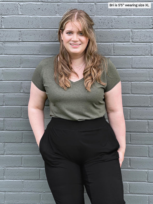 Woman standing in front of a brick wall wearing Miik's Silvie slouch pant in black with a sage melange v neck tee