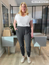 Woman standing in an office wearing Miik's Silvie slouch pant in charcoal with a basic white tee 