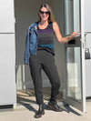 Woman opening the door wearing Miik's Silvie slouch pant in charcoal along with a striped tank top, boots and sunglasses