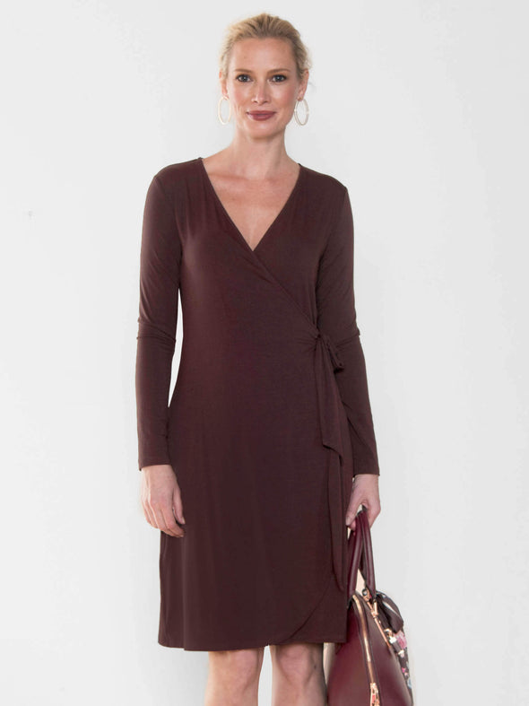 Model standing in front of a white wall wearing Miik's Sonya wrap dress in dark chocolate