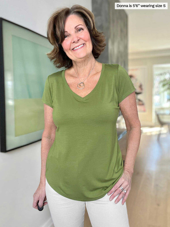 Miik founder Donna (five foot six, size small) wearing Sutton classic v-neck t-shirt in moss green with white jeans while smiling in a high-end living room.