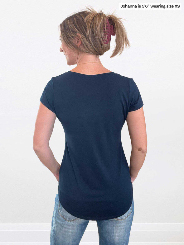 Woman standing in front of a wall with her back towards the camera wearing Miik's Sutton v-neck classic tee in navy with jeans.