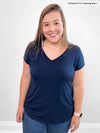 Woman standing in front of a white wall smiling wearing Miik's Sutton v-neck classic tee in navy with jeans.