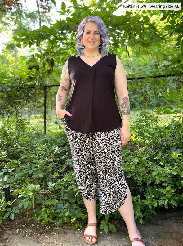 Woman smiling standing in a backyard wearing Miik's Taz sleeveless inverted pleat top in black along with a capri pant  in animal print