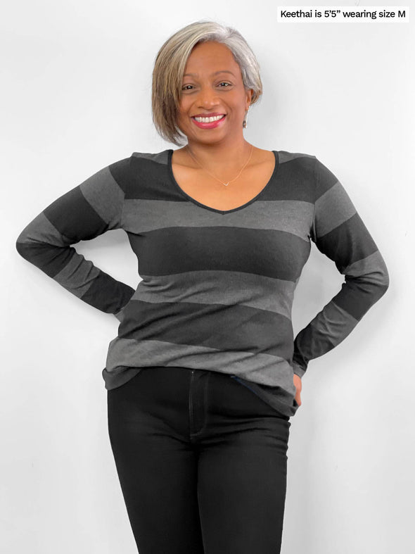 Woman standing in front of a wall wearing Miik's Tray long sleeve striped tee in grey stripe with jeans.