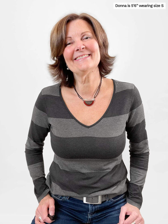 Woman standing in front of a wall wearing Miik's Tray long sleeve striped tee in grey stripe with jeans.