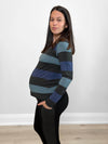 Pregnant woman standing in front of a wall wearing Miik's Tray long sleeve striped tee in blue stripe with black leggings.