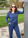 Woman standing next to a brick wall smiling while wearing Miik's Tula long sleeve open-back jumpsuit in navy melange