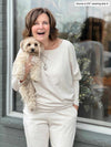 Woman smiling while holding a dog wearing  Miik's Tully reversible fleece dolman sweater in oatmeal melange with a fleece jogger in the same colour 