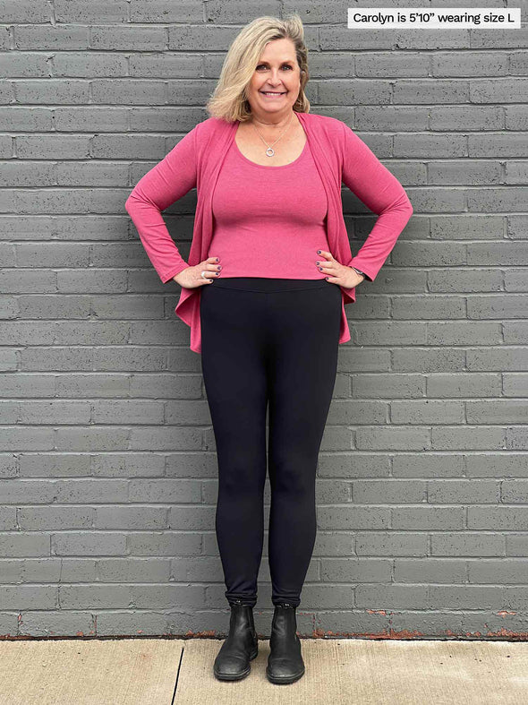 Woman standing in front of a brick wall wearing Miik's Tyson fleece legging in black with a pink pomegranate top with a matching colour waterfall cardigan