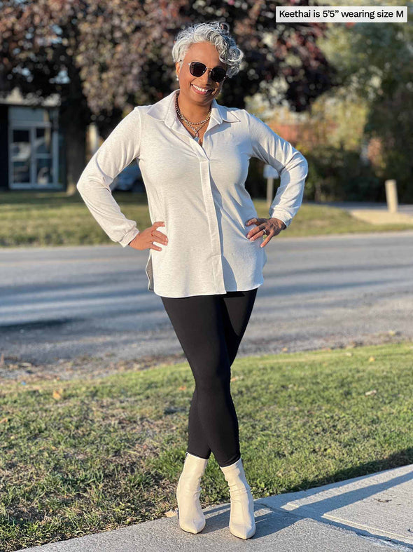 Woman smiling standing in a sidewalk wearing Miik's Tyson fleece legging in black with a collared shirt in oatmeal, sunglasses and boots.