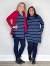 Two women standing in front of a white wall wearing Miik's Venice cowl pocket tunic in navy jewel tone stripe along side with navy leggings