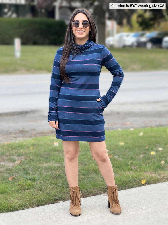 Woman smiling while standing in a sidewalk wearing Miik's Venice cowl pocket tunic in navy jewel tone stripe with boots and sunglasses