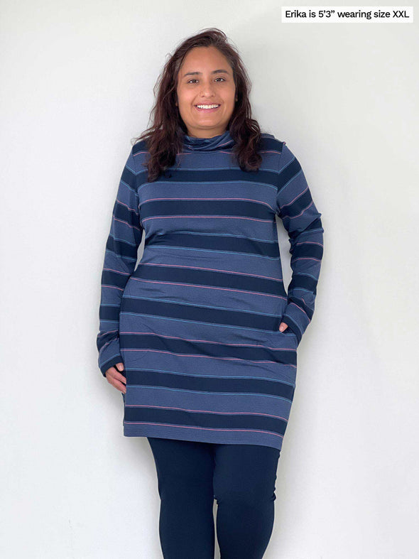 Woman standing in front of a white wall with her hand in one of the pockets of the Miik's Venice cowl pocket tunic in navy jewel tone stripe