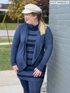 Woman smiling and looking away wearing Miik's Venice cowl pocket tunic in navy jewel tone stripe with a navy melange waterfall cardigan and leggings