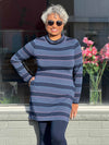 Woman standing in front of a window wearing Miik's Venice cowl pocket tunic in navy jewel tone stripe, navy legging and sunglasses 