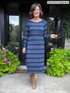 Woman standing in a doorway while wearing Miik's Verona long sleeve boat neck dress in navy jewel tone stripe and boots