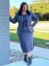 Woman standing next to a brick wall wearing Miik's Verona long sleeve boat neck dress in navy melange with a matching colour blazer
