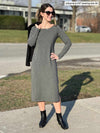 Woman standing on a sidewalk wearing Miik's Verona long sleeve boat neck dress in granite melange with a black blazer on her shoulder and black boots