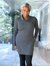 Woman standing in a room wearing Miik's Vienna cowl pocket tunic in granite melange with black legging