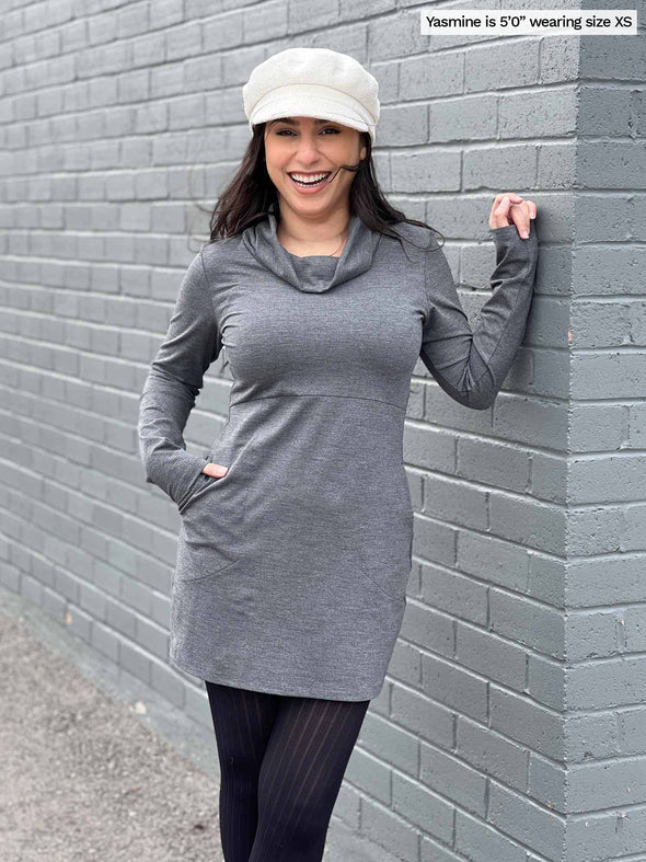 Woman smiling leaning against a brick wall wearing Miik's Vienna cowl pocket tunic in granite melange